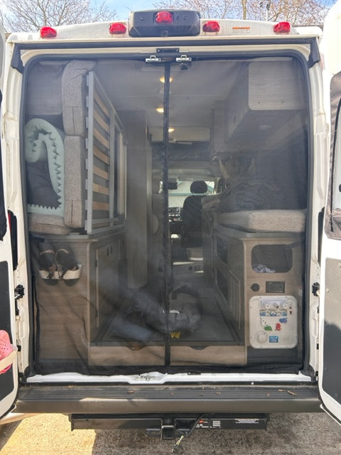 RV rental's rear view through mesh: a packed interior with bed frame, cushions, and control panel.