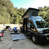 Enjoying an **RV rental** adventure! A pop-top camper van is set up at a rustic campsite with a dog, picnic area, and trees.