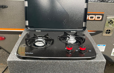 Outdoor Suburban gas stove with black burners and red control knobs, attached to an RV rental camper for convenient cooking.