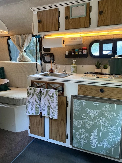 This cozy RV rental interior features a compact kitchen with sink, stovetop, and fridge, plus a comfy bench seat. — photo 6