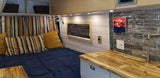This RV rental interior features a cozy bed, sleek kitchen with wood counters & tiled backsplash, plus custom storage.