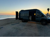 Experience van life with an RV rental! A dark gray camper van parked beachfront at sunset, doors open to ocean views.