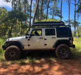 This silver Jeep Wrangler, perfect for an RV rental outdoor adventure, is parked on a forest trail with a dog in the driver's seat.