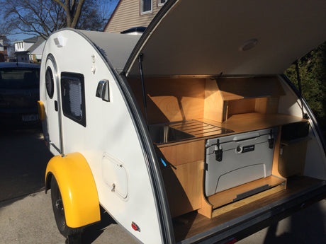 Explore this white teardrop camper's open rear galley with sink & cooler – ideal for RV rental vacations.