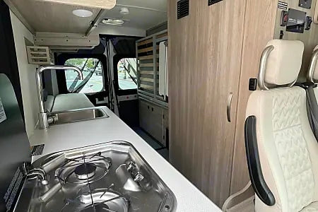 Modern RV rental interior: kitchen with sink & stove, ample storage, and comfortable front seats.