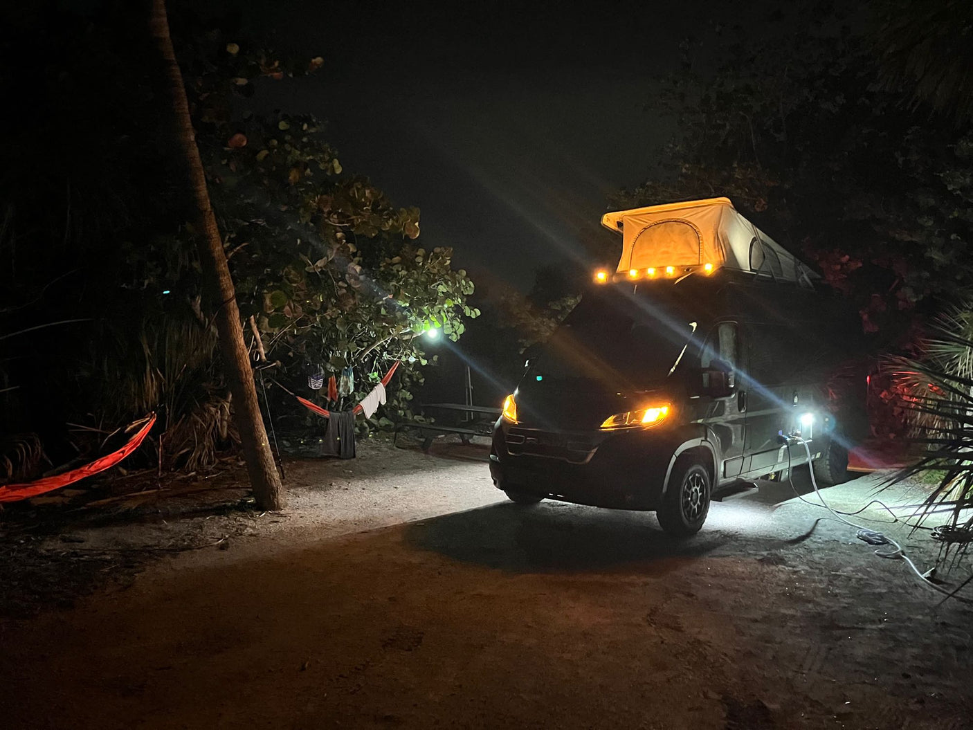 Nighttime RV rental adventure with illuminated pop-top tent, hammock, and campsite lights.