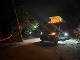 Nighttime RV rental adventure with illuminated pop-top tent, hammock, and campsite lights.