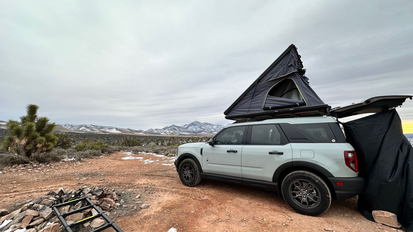  plus a Heytrip gear bag.|Desert camping with an RV rental: An SUV with a pop-up rooftop tent sits amidst mountains. People relax — photo 5