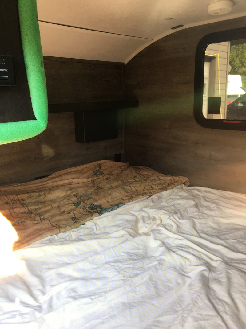 An rv rental bedroom features a cozy bed with a map blanket, white sheets, and warm wooden interior walls. — photo 13
