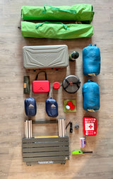 Camping gear laid out for an RV rental trip: stove, cookware, sleeping bags, pillows, and first aid supplies.
