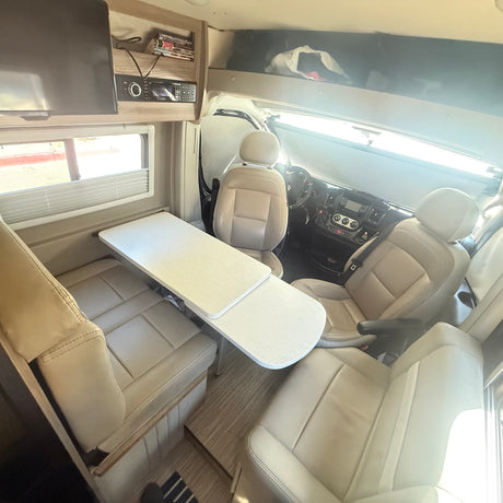 Comfortable rv rental interior: cream seating, dining table, and driver's cabin. Ideal camper living space.