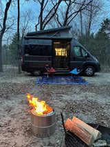 Cozy evening at the rv rental campsite. Pop-top camper van, bright fire pit, chairs on a mat, and logs ready.