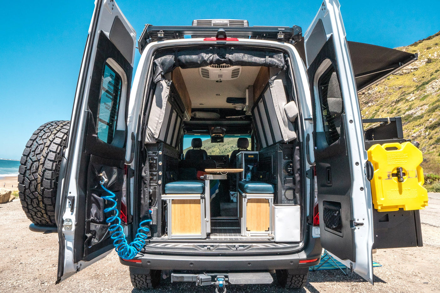 Explore with this RV rental camper van! Rear doors open, revealing custom interior, outdoor shower, spare tire, and fuel can. — photo 7