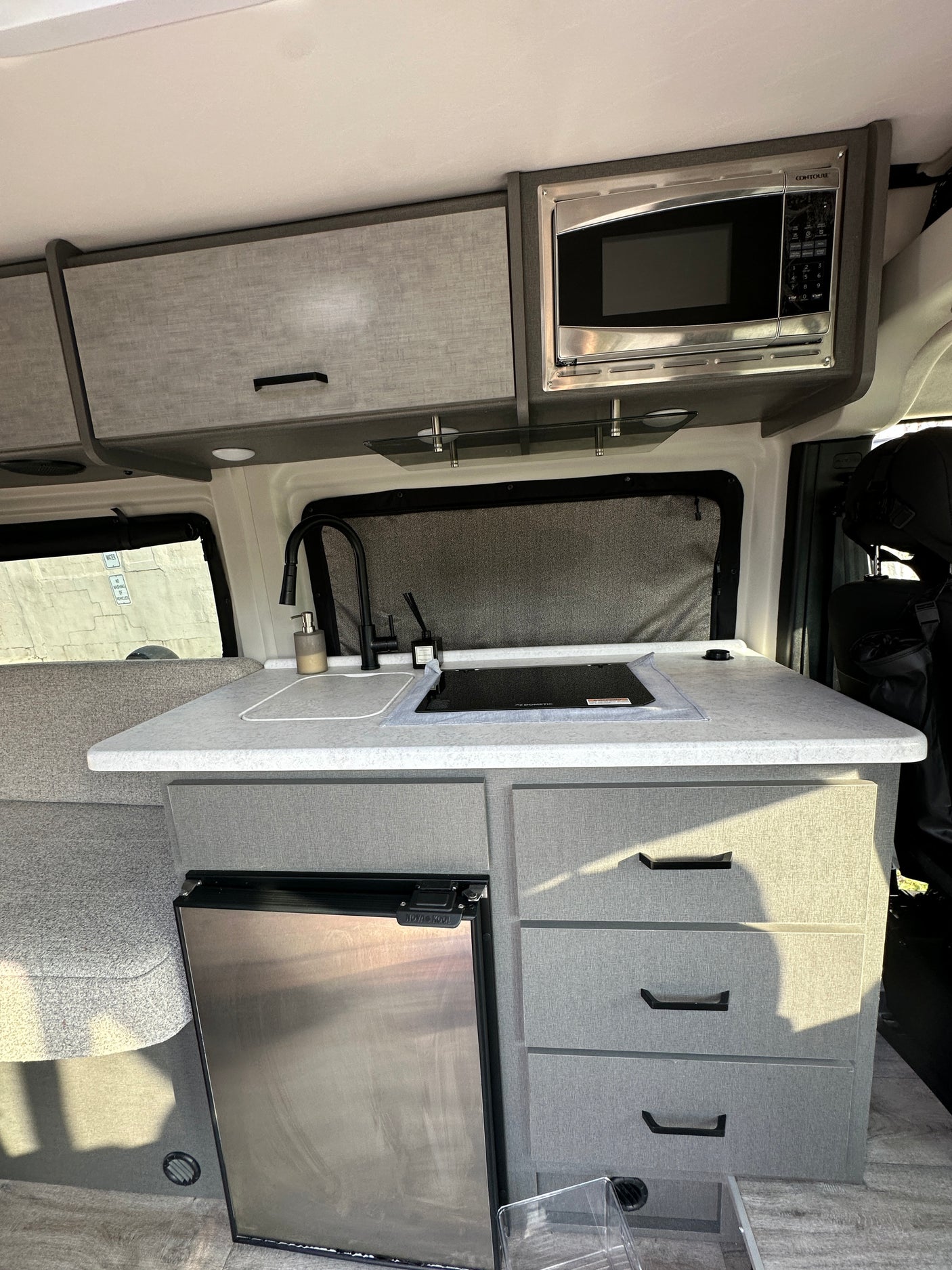 RV rental kitchen: compact, well-equipped galley with sink, cooktop, microwave, fridge, and ample storage.