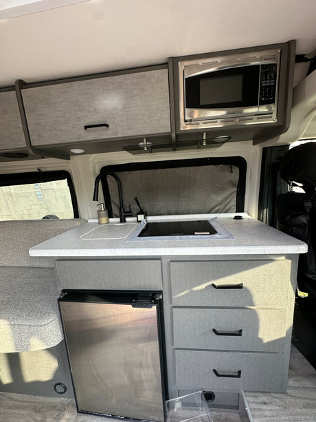 RV rental kitchen: compact, well-equipped galley with sink, cooktop, microwave, fridge, and ample storage.