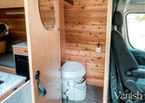 Compact RV rental interior featuring a cedar-paneled composting toilet area with a small mirror, plus a glimpse of the kitchenette.