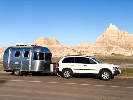 RV rental: A sleek Airstream trailer towed by a white Volvo SUV, set against the striking Badlands formations.