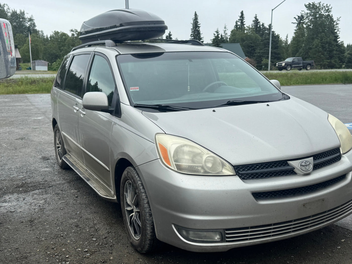  surrounded by tall evergreen trees.|Silver Toyota Sienna minivan with cargo box & boat — photo 13