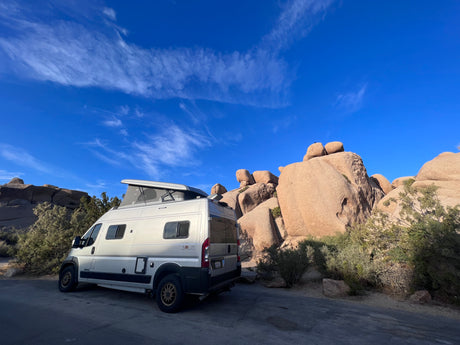Explore stunning landscapes! An RV rental camper van parked amidst iconic rock formations and desert plants under a clear blue sky.