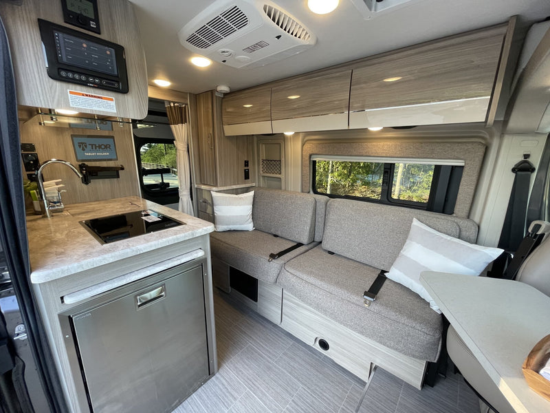 Modern RV rental interior featuring a well-equipped kitchenette, comfortable seating with a table, and smart control panel. — photo 9