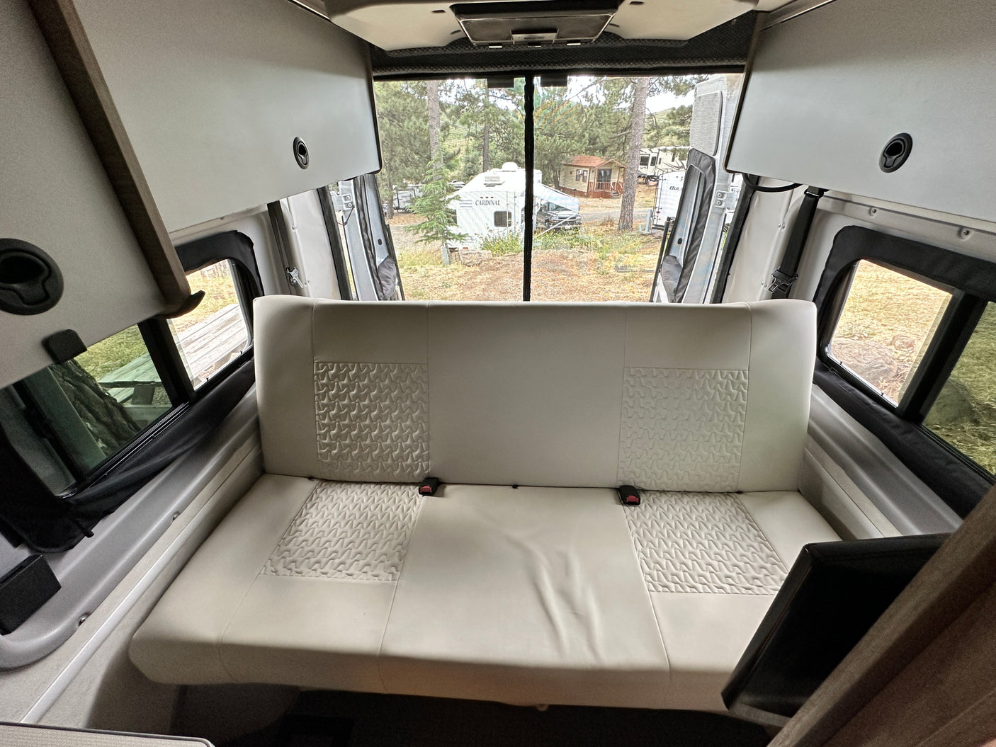 Spacious rv rental interior featuring a comfy bench seat, overhead storage, and views of a peaceful campground.