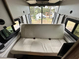 Spacious rv rental interior featuring a comfy bench seat, overhead storage, and views of a peaceful campground.