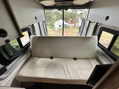 Spacious rv rental interior featuring a comfy bench seat, overhead storage, and views of a peaceful campground.