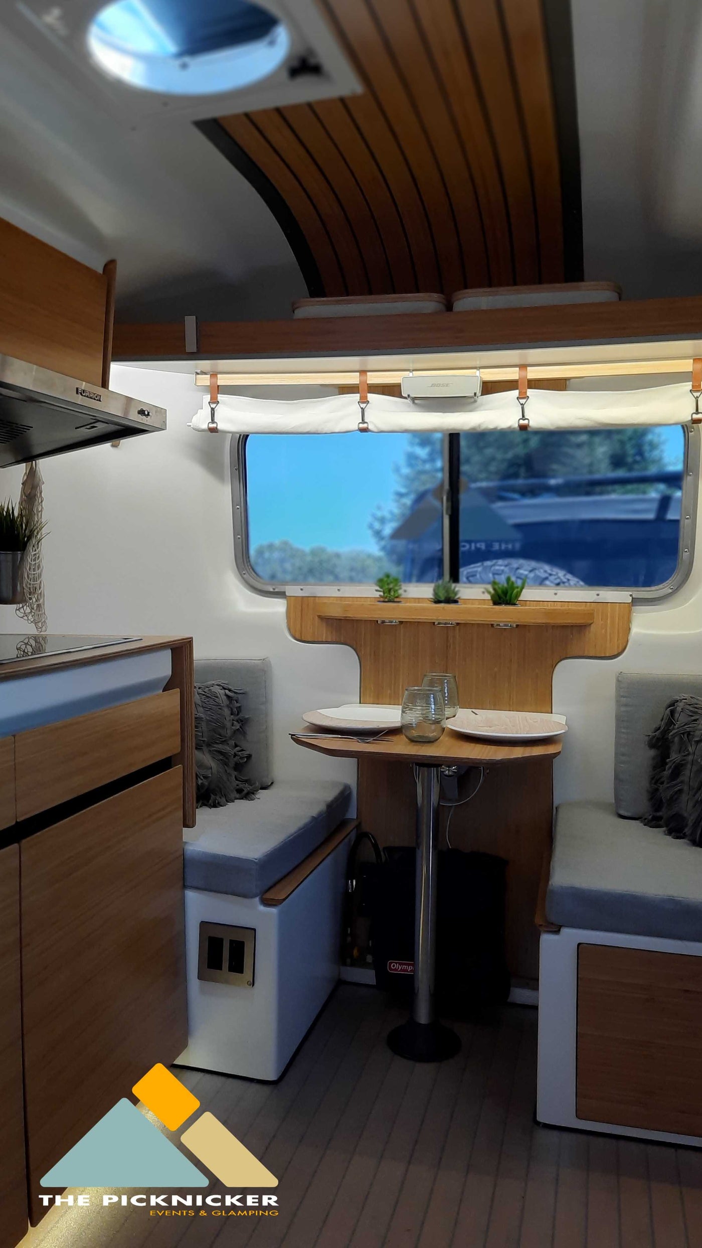 Modern RV rental interior with a cozy kitchen and dining area. Wood accents & large window offer a bright, comfortable space. — photo 11