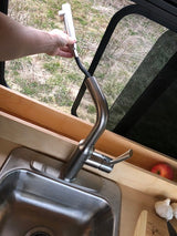 RV rental kitchen: Hand extends pull-down faucet sprayer out window, showing compact sink, counter with apple & garlic.