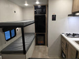 RV rental interior showcasing bunk beds, a compact kitchen with a stove, and built-in appliances like a microwave and fireplace.