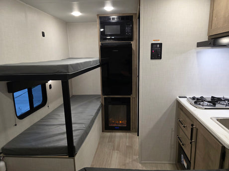 RV rental interior showcasing bunk beds, a compact kitchen with a stove, and built-in appliances like a microwave and fireplace.