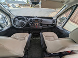 Explore the comfortable interior of this RV rental, featuring the driver's cockpit, spacious dashboard, and tan leather seats.