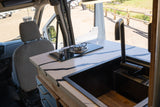 Inside an RV rental, a compact kitchen features a stylish counter, stove, and sink, visible from the passenger seat.