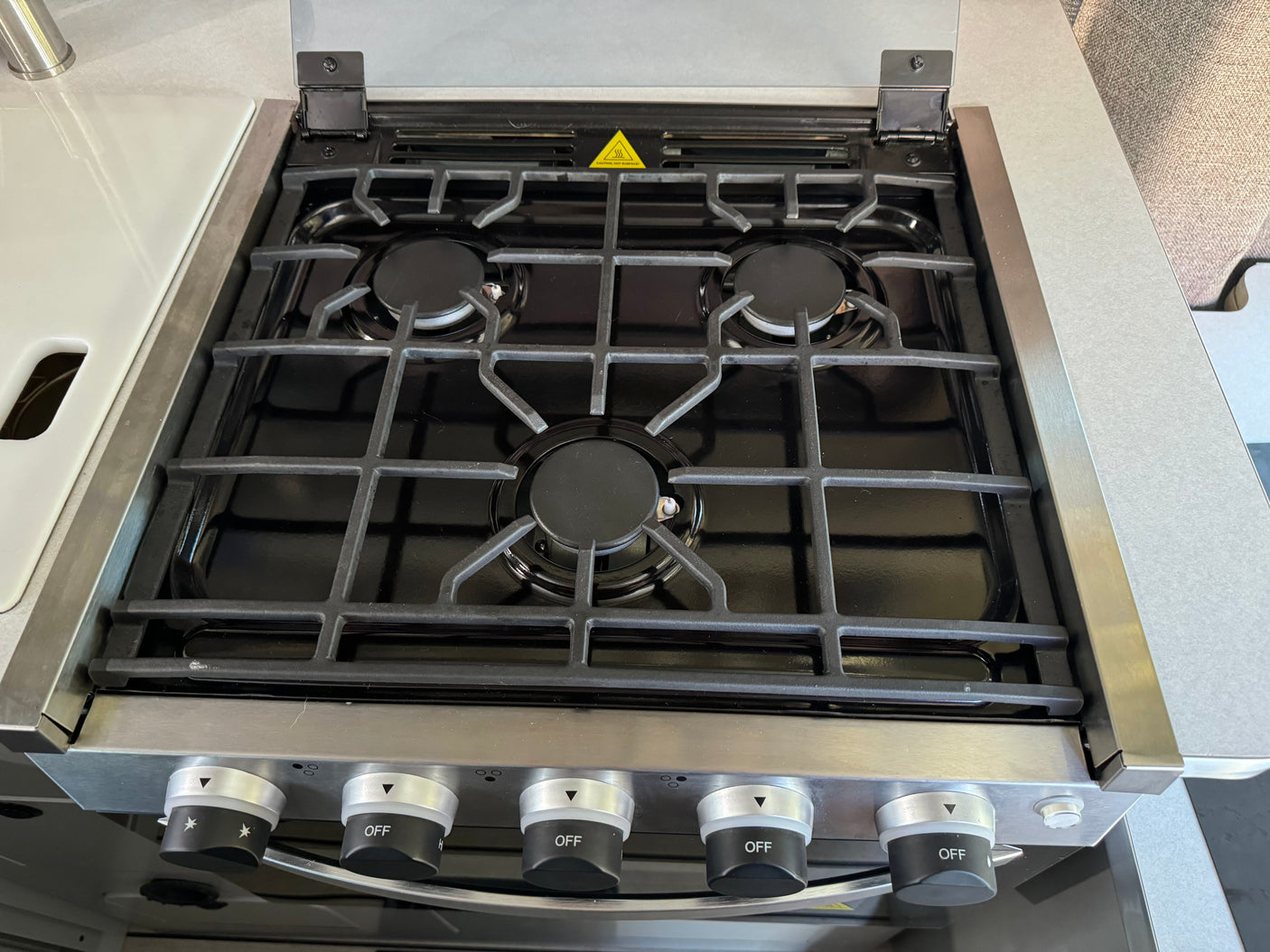Three-burner gas stove with black grates and control knobs in an rv rental kitchen. Ideal for convenient travel cooking.