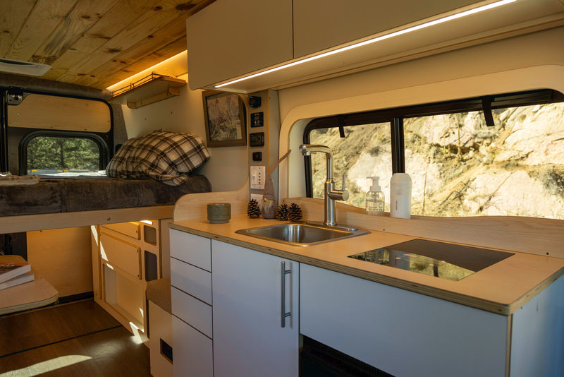 Modern rv rental interior showcasing a cozy bed, full kitchen with a sink and cooktop, and clever built-in storage. — photo 15