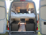 This RV rental camper van's custom interior reveals an elevated bed with lighting, over large lower storage units.