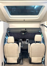 Forward view inside an RV rental showing light-colored front seats, dashboard, and a sunshade. A large skylight is above.