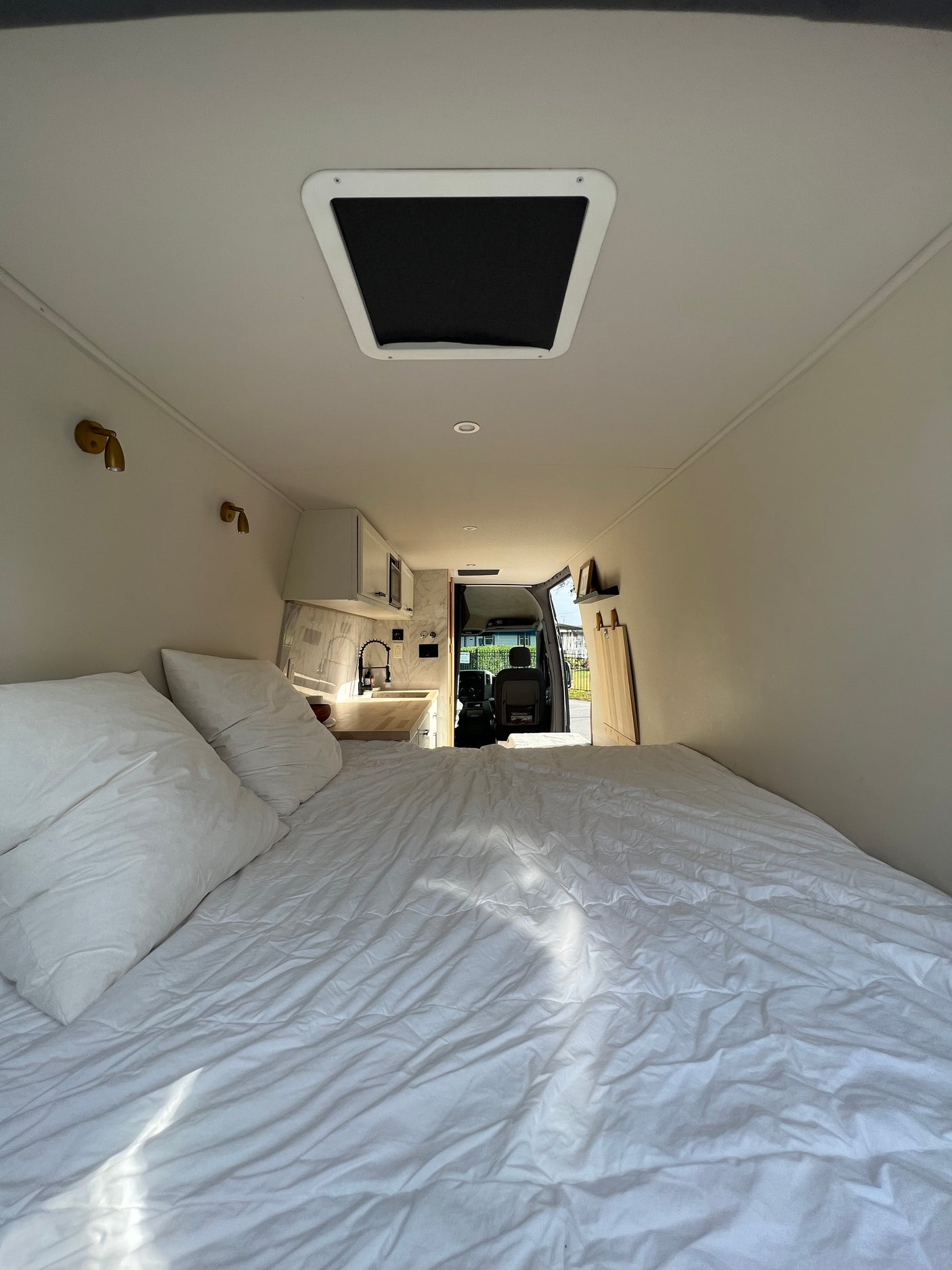 Inside a comfortable RV rental: white bedding, compact kitchen, and open driver's cabin. Ready for the road.