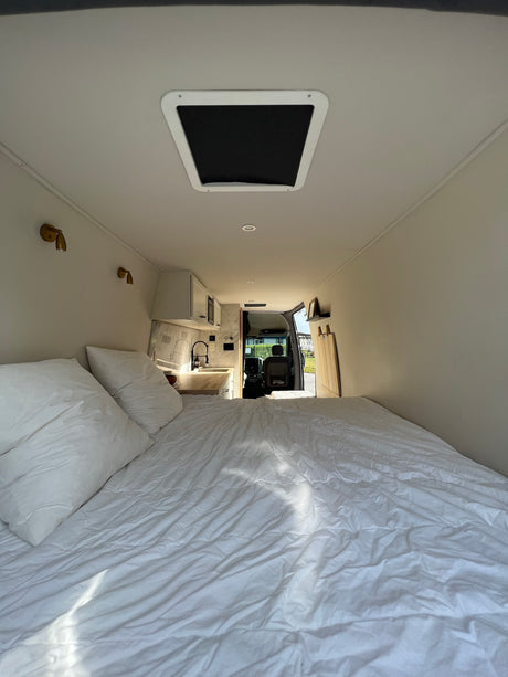 Inside a comfortable RV rental: white bedding, compact kitchen, and open driver's cabin. Ready for the road.