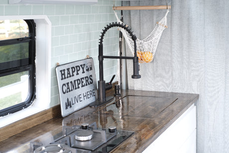 Cozy RV rental kitchen with wood counters, modern faucet, and a "Happy Campers" sign. Oranges in a net.
