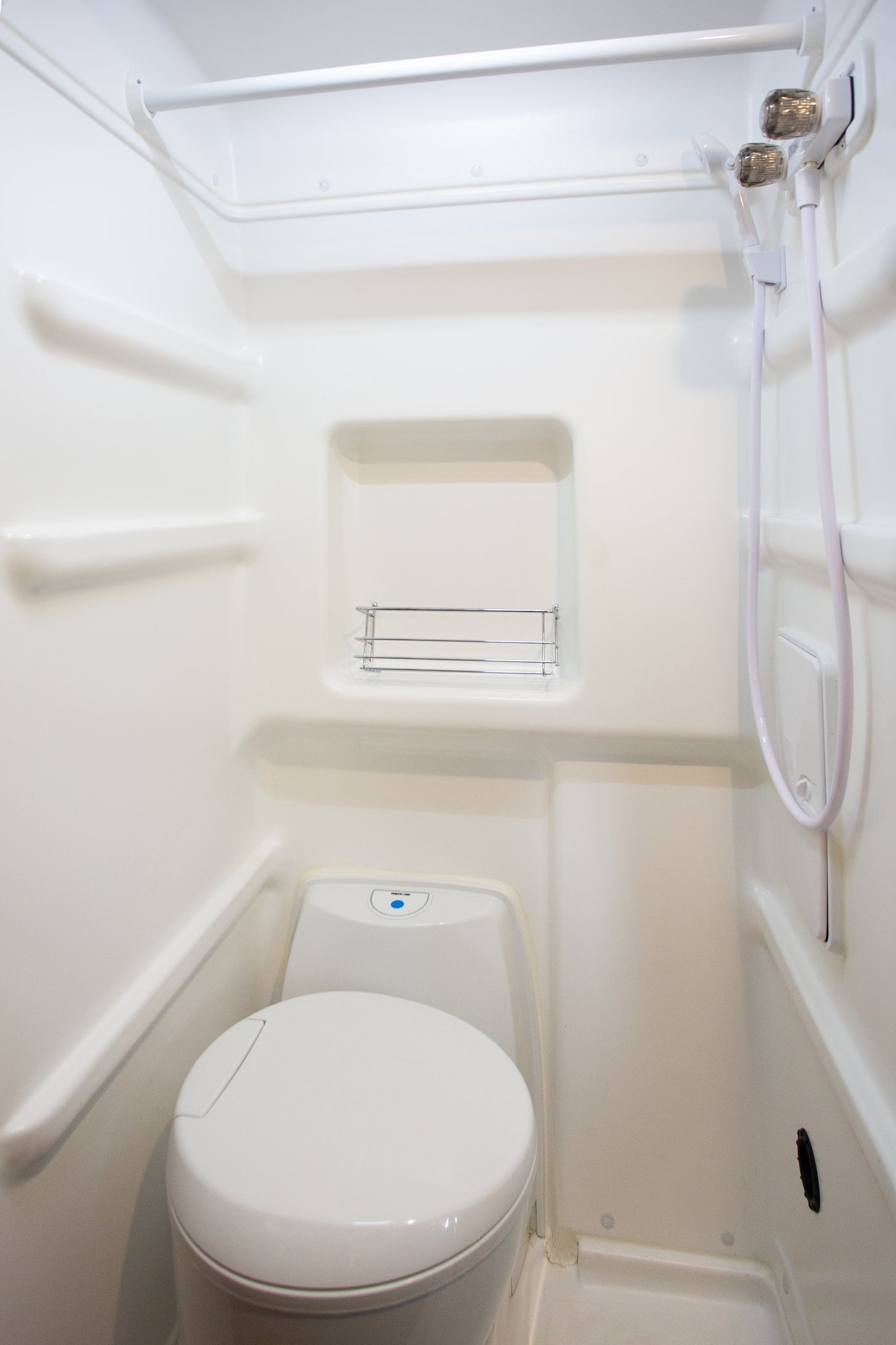Compact white RV bathroom with integrated toilet, shower, and shelving, ideal for an rv rental.