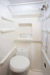 Compact white RV bathroom with integrated toilet, shower, and shelving, ideal for an rv rental.