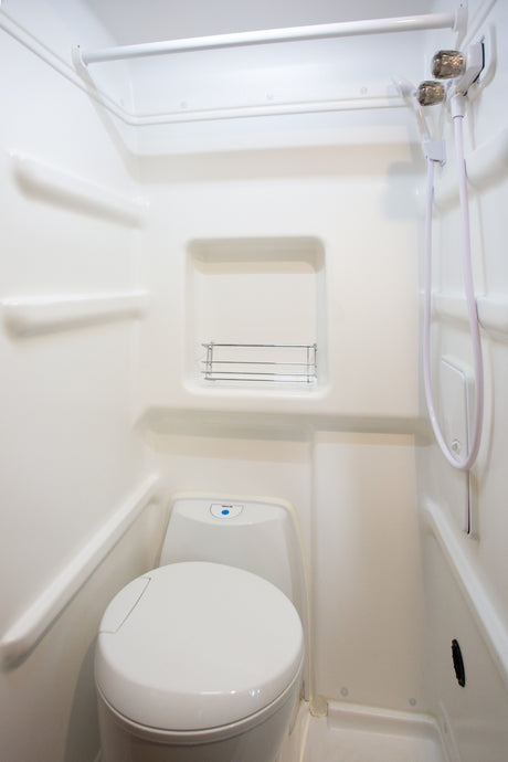 Compact white RV bathroom with integrated toilet, shower, and shelving, ideal for an rv rental.