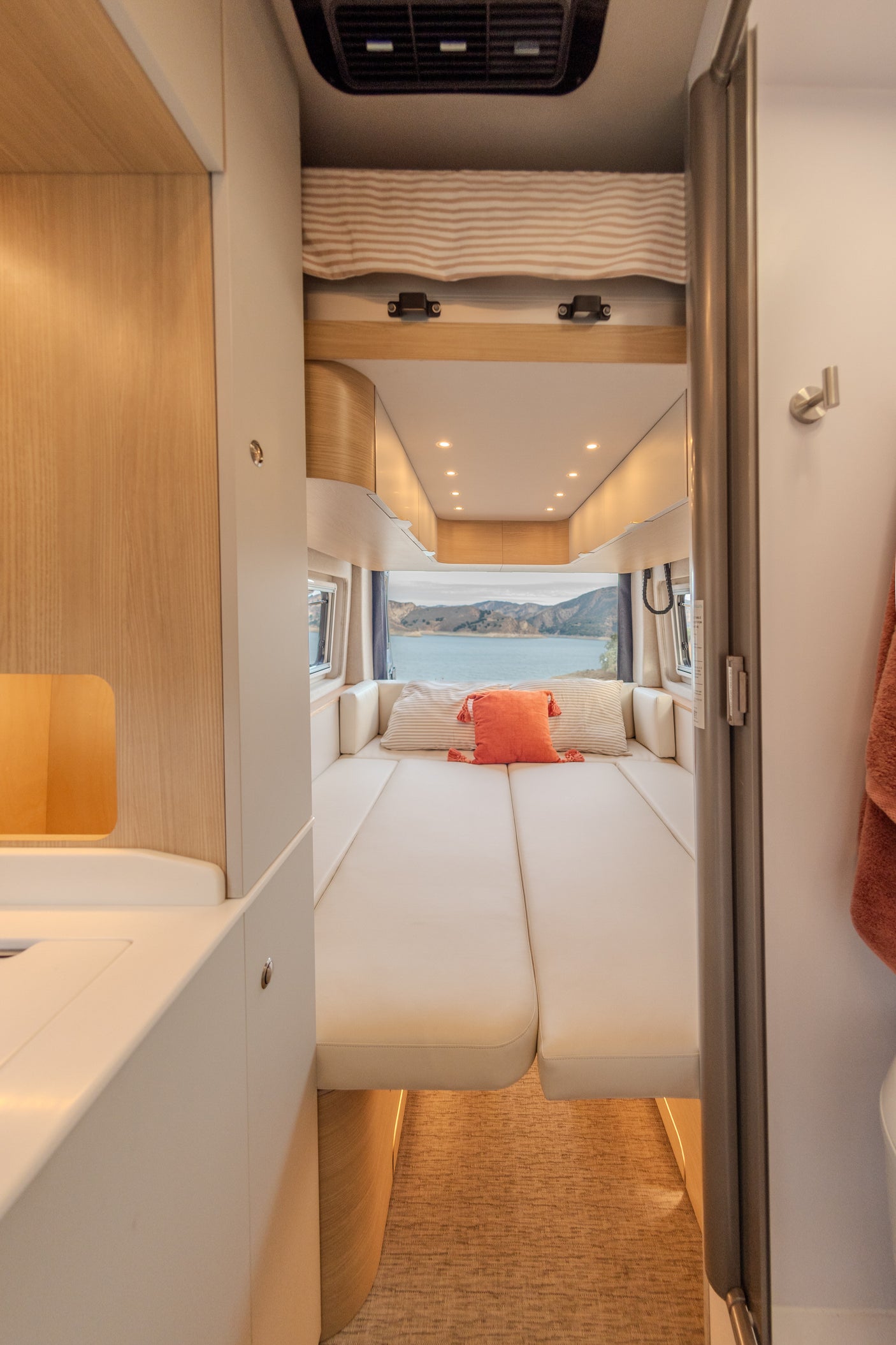 This RV rental interior offers a cozy bedroom with a stunning lake and mountain view, featuring comfortable cushions and modern amenities.