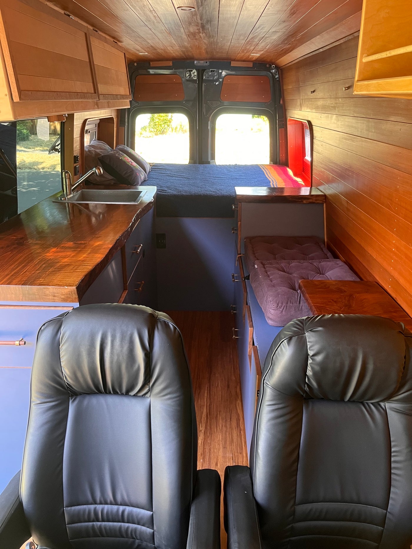 Cozy rv rental interior with wood paneling, black leather seats, a bed, and kitchenette – ideal for travel. — photo 2