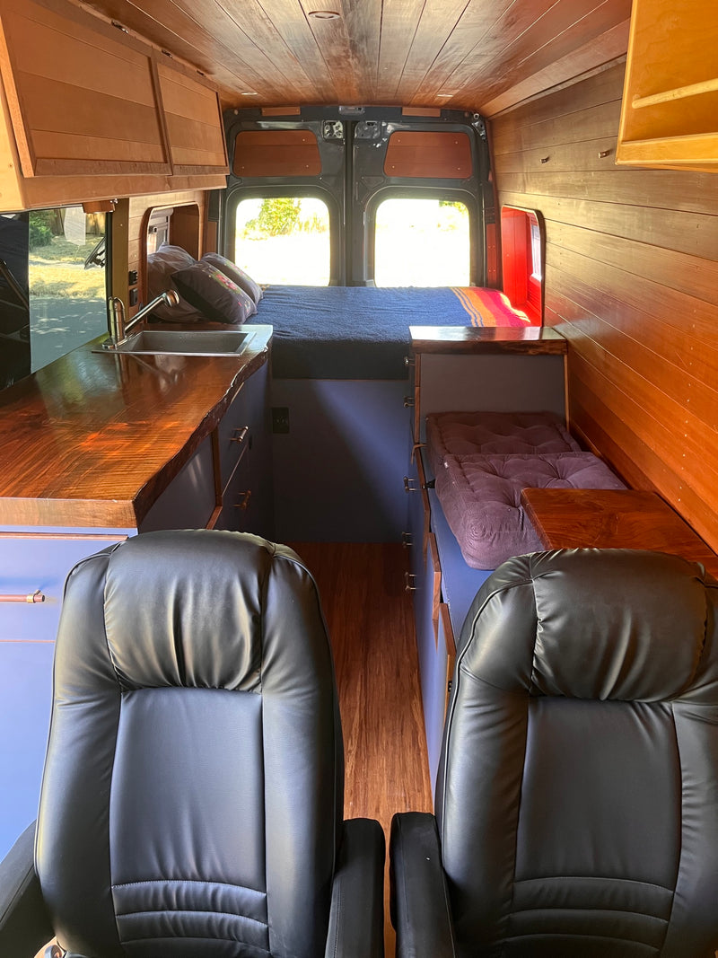 Cozy rv rental interior with wood paneling, black leather seats, a bed, and kitchenette – ideal for travel. — photo 2