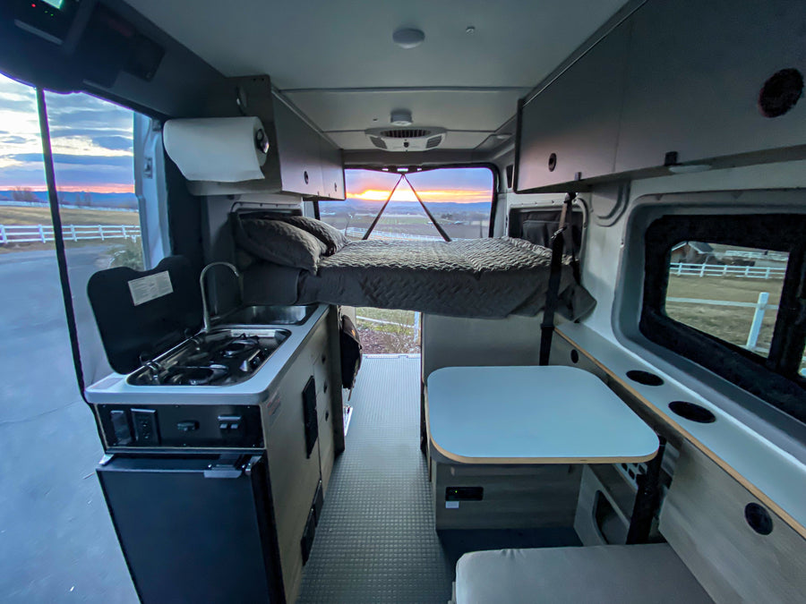 Inside a spacious RV rental: full kitchen, elevated bed, and dining area with a beautiful sunset view from the back.