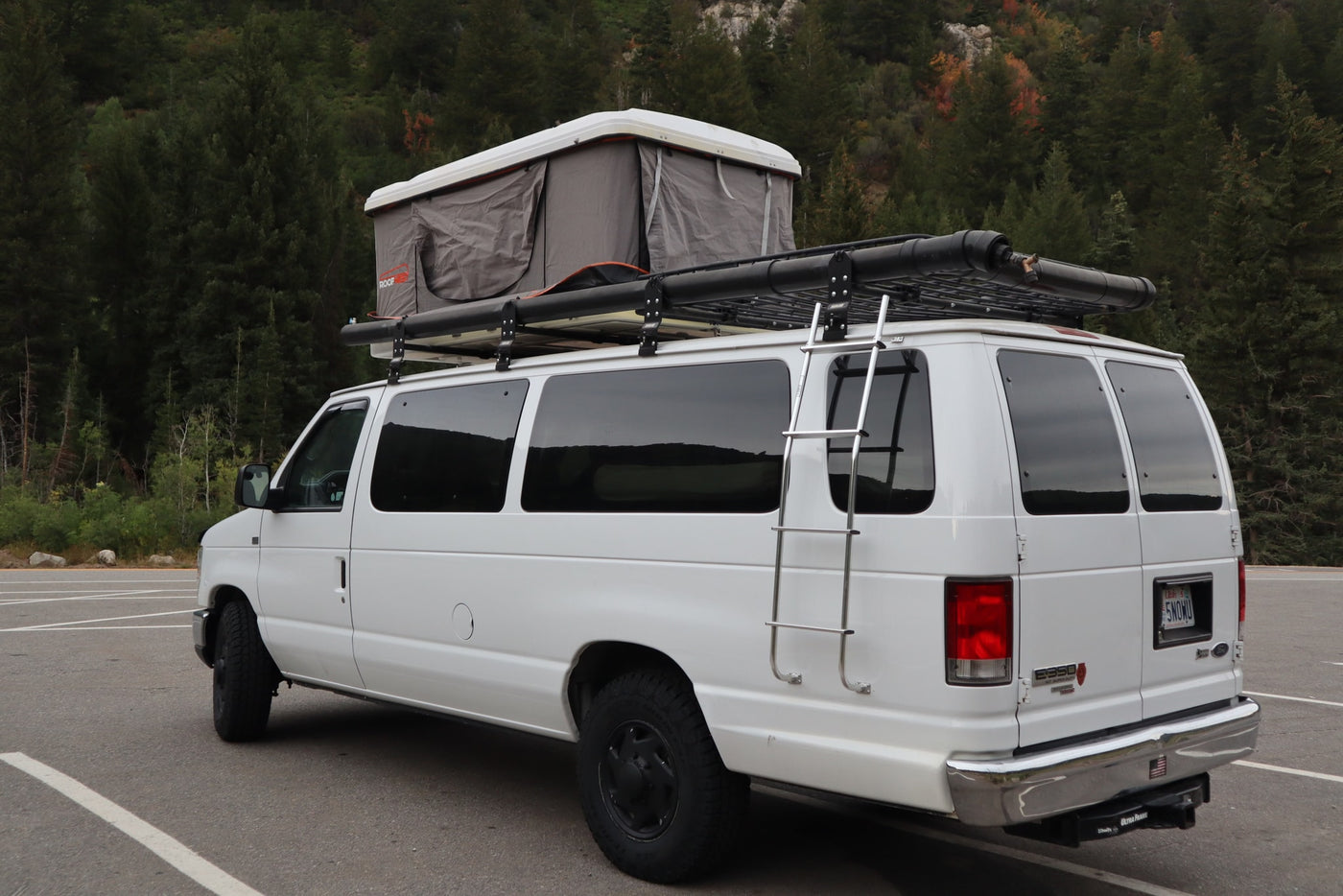 White adventure van with rooftop tent and roof rack, parked in nature. An ideal rv rental for outdoor camping trips. — photo 8