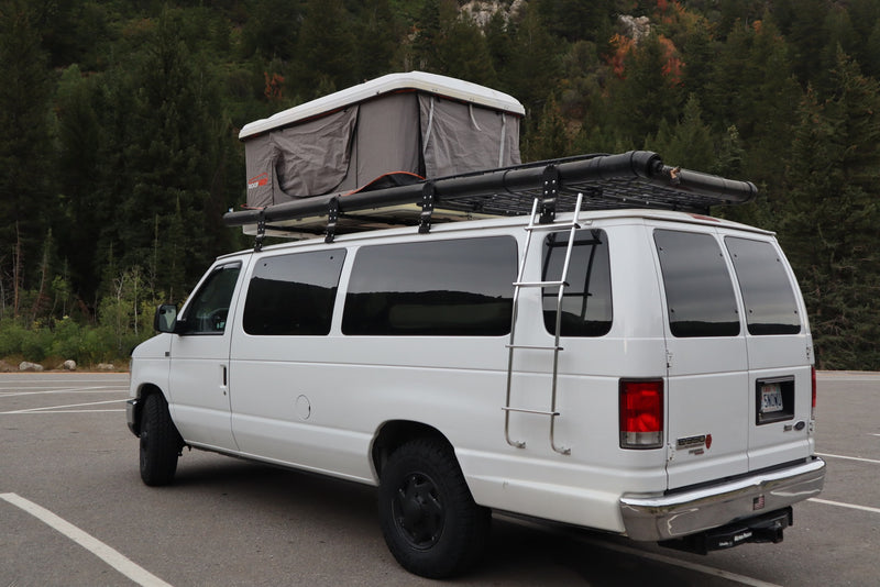 White adventure van with rooftop tent and roof rack, parked in nature. An ideal rv rental for outdoor camping trips. — photo 8