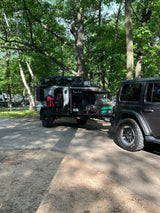 Rugged gray Jeep pulls a black 'Houtla Rentals' overland camper trailer, an ideal RV rental for outdoor trips.